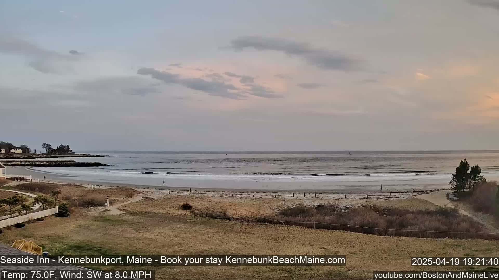 A sandy beach with gentle waves and a calm ocean under a mostly cloudy, pastel sky.