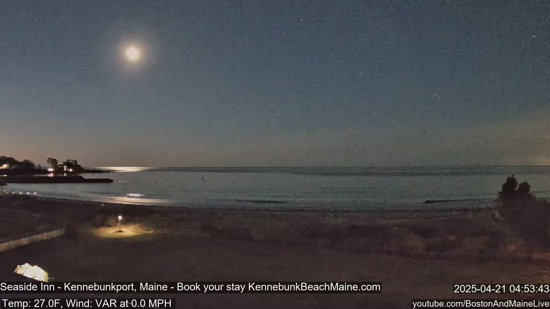 A bright moon illuminates a calm, dark ocean beach at night.