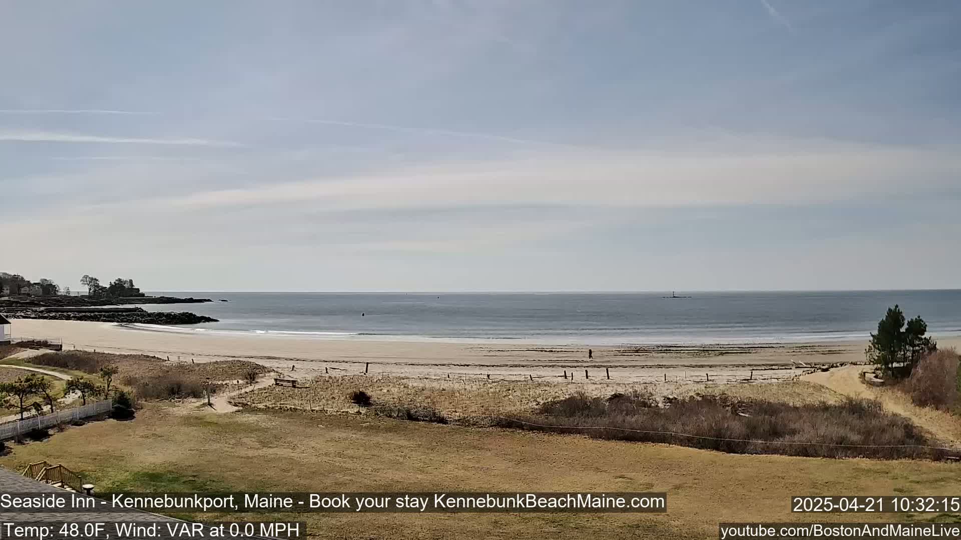A sandy beach stretches along a calm ocean under a mostly clear sky.