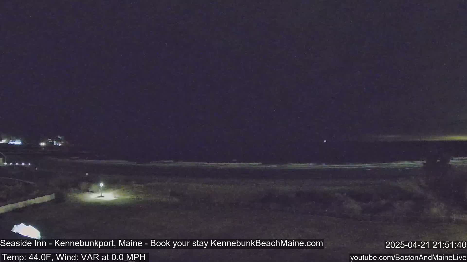 A nighttime view of a dark beach with calm waves under a clear, dark sky.
