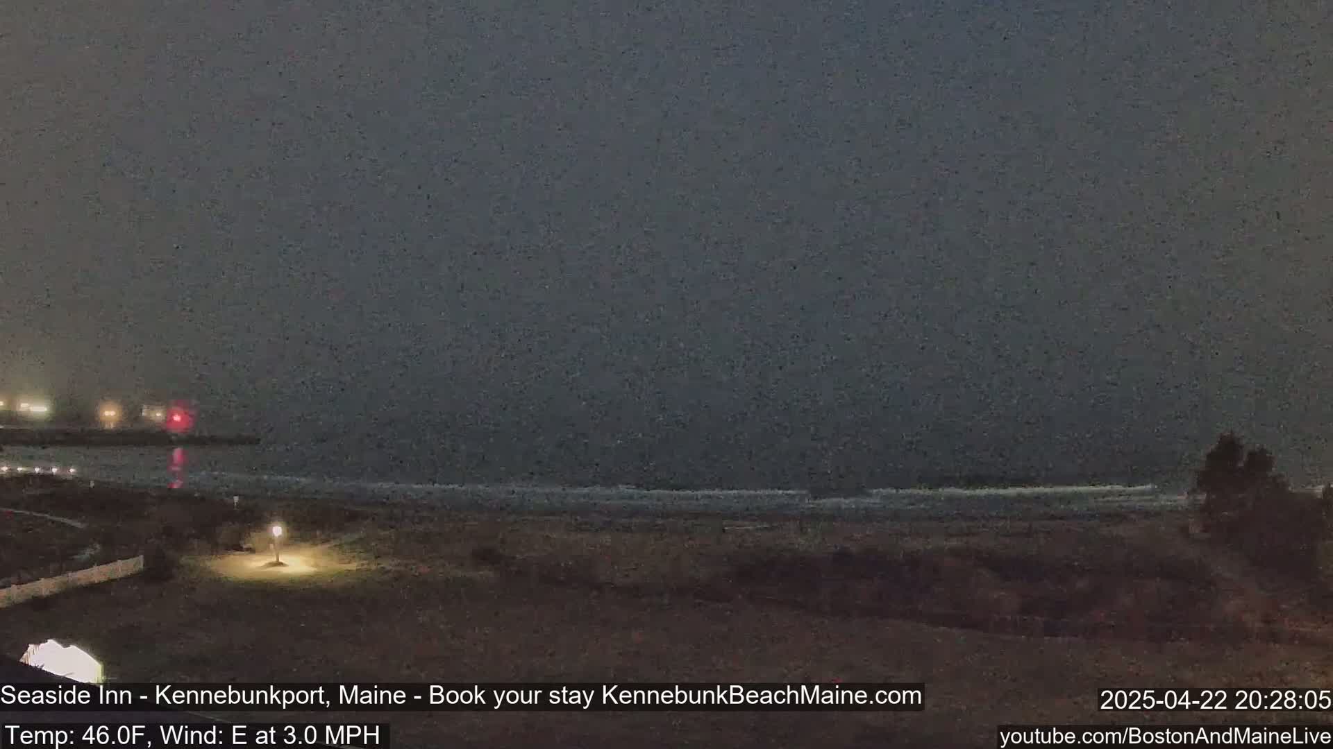 A dark, foggy beach scene at night shows a calm ocean with a few small waves under a dark sky.