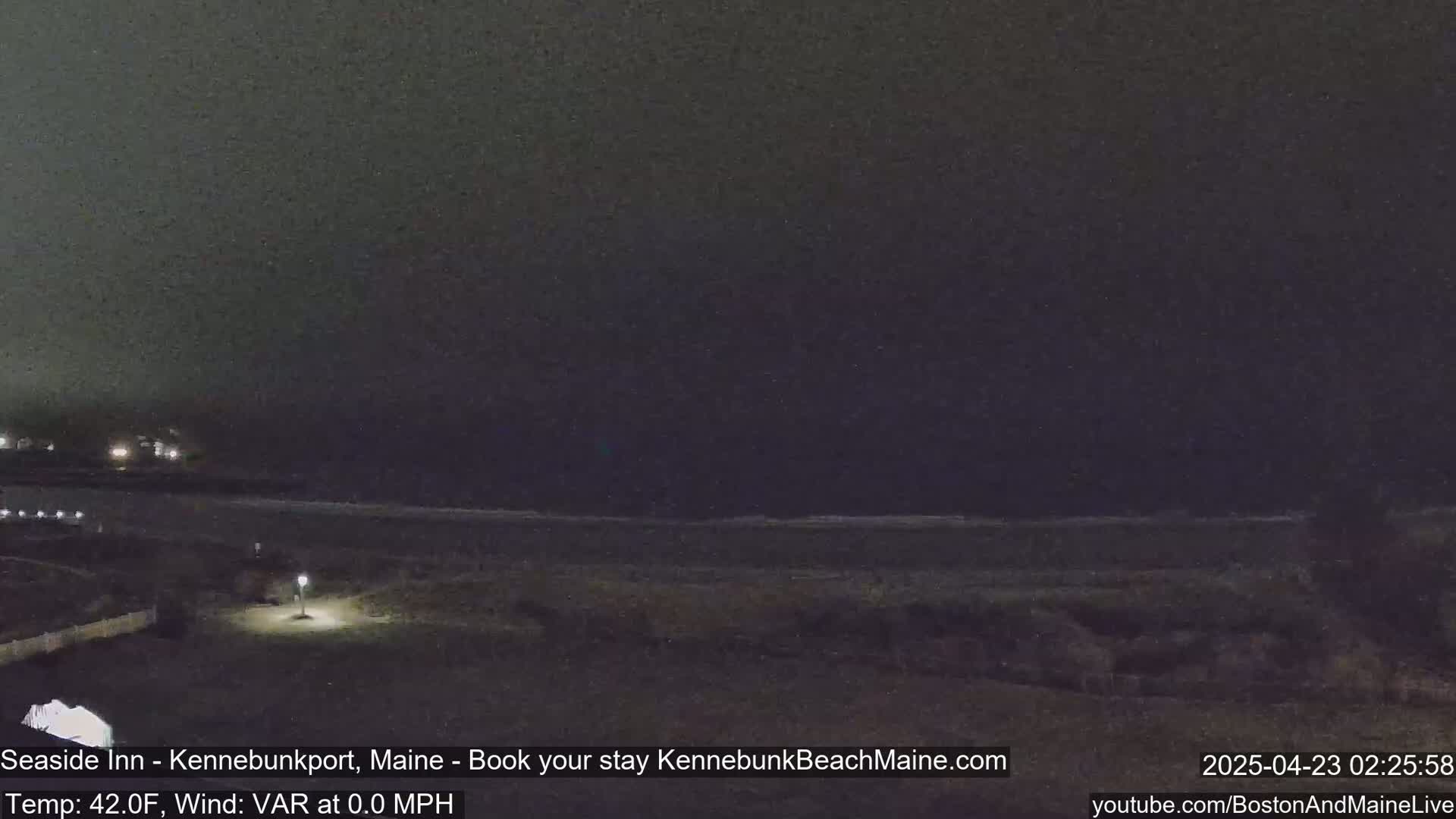 A dark, nighttime beach scene shows a calm ocean under a mostly clear sky.