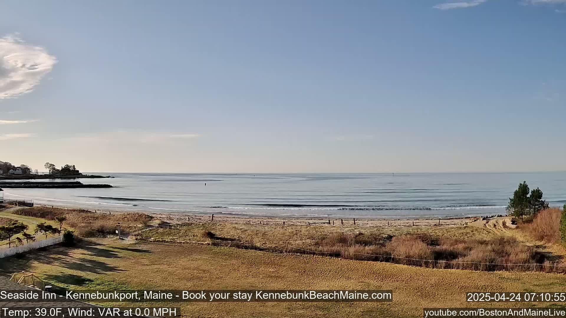 A sandy beach with calm ocean waves stretches out under a mostly clear, light blue sky.