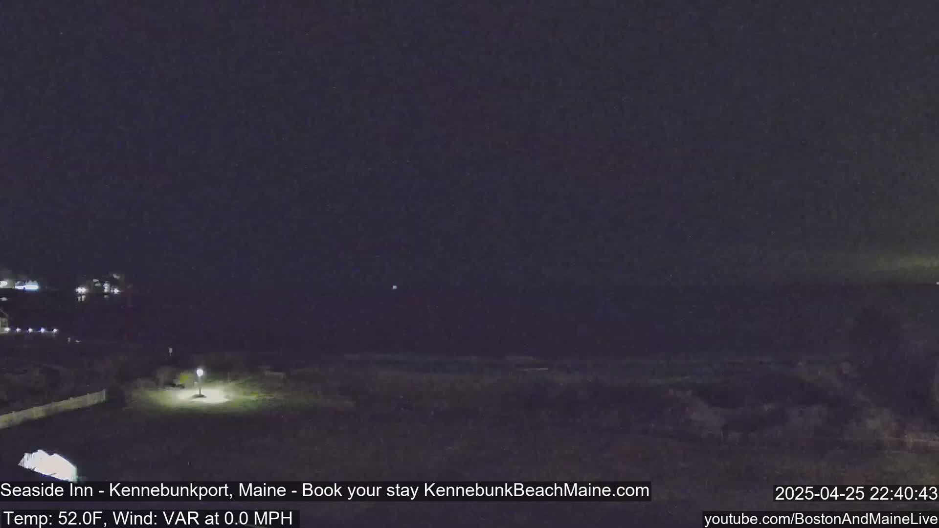 A nighttime view of a dark beach with a single lit lamppost, and some distant lights visible.