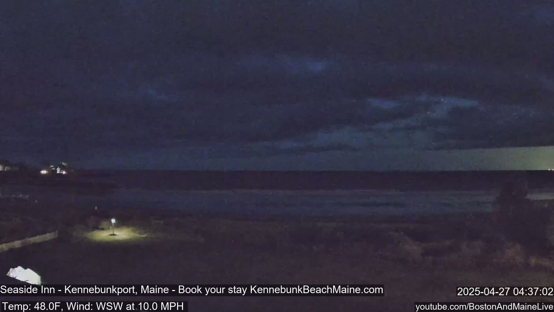 A dark, nighttime coastal scene shows a calm ocean under a mostly cloudy sky with a gentle WSW wind.