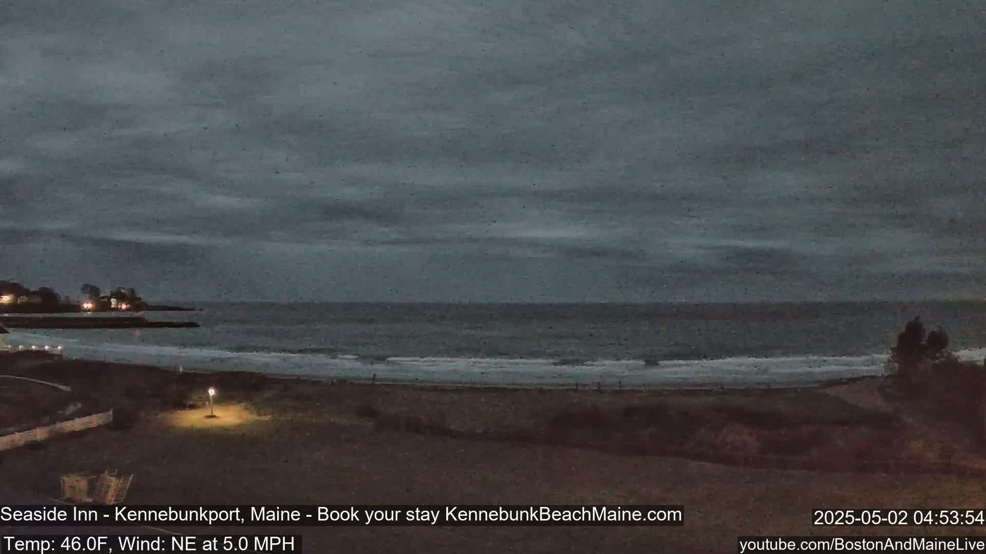 A dark, overcast evening scene shows a beach with gentle waves lapping the shore under a gray sky.