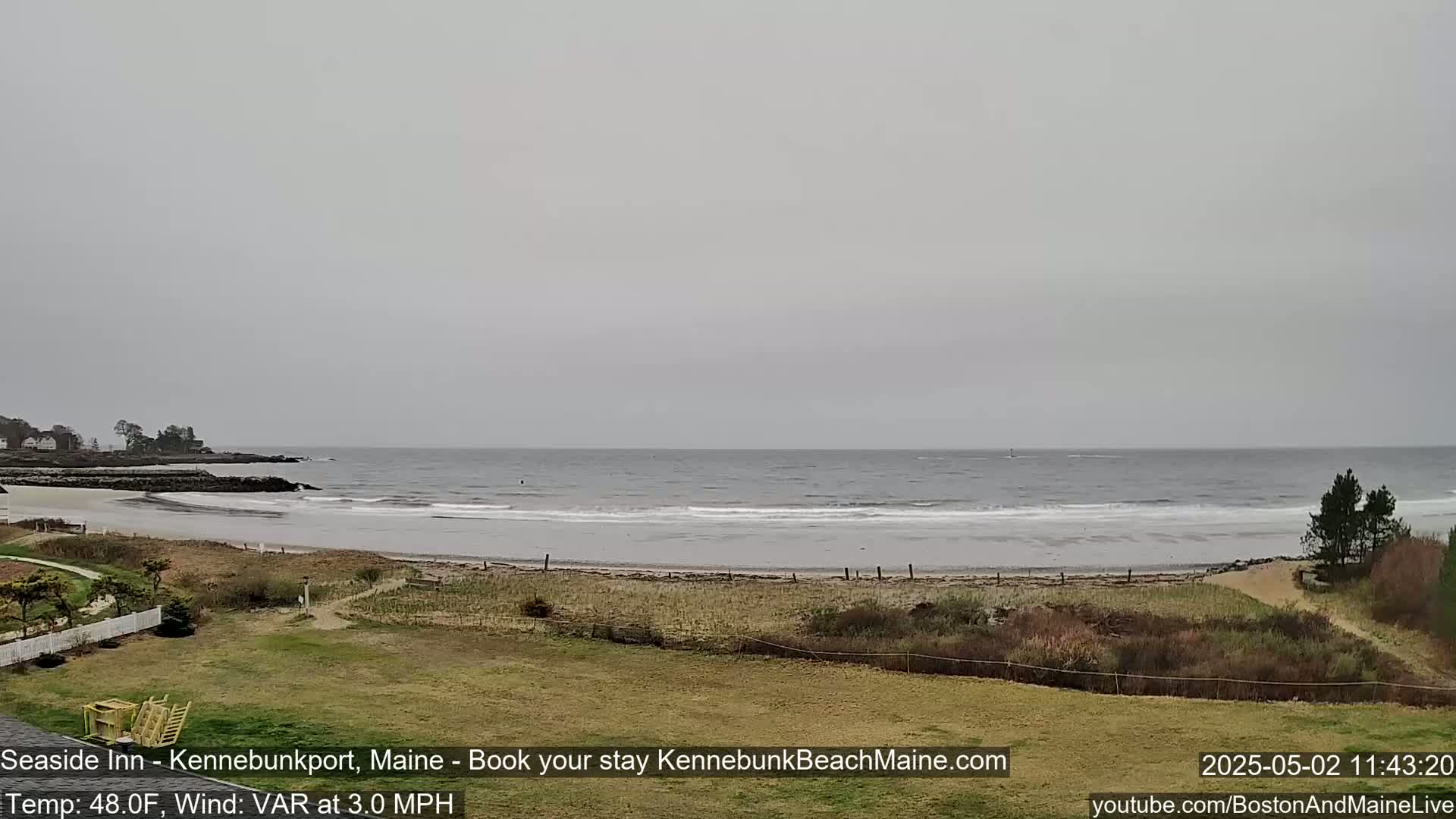 A view of a sandy beach and calm ocean under an overcast sky.