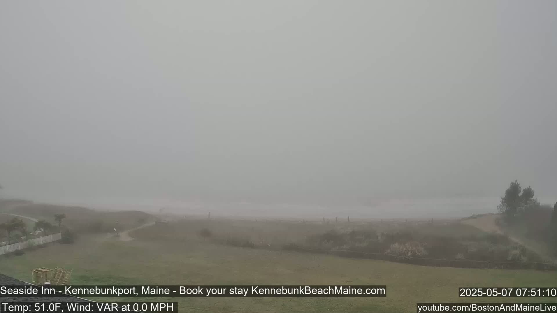 A foggy, calm beach scene is visible from a grassy area, with a glimpse of the ocean in the distance.