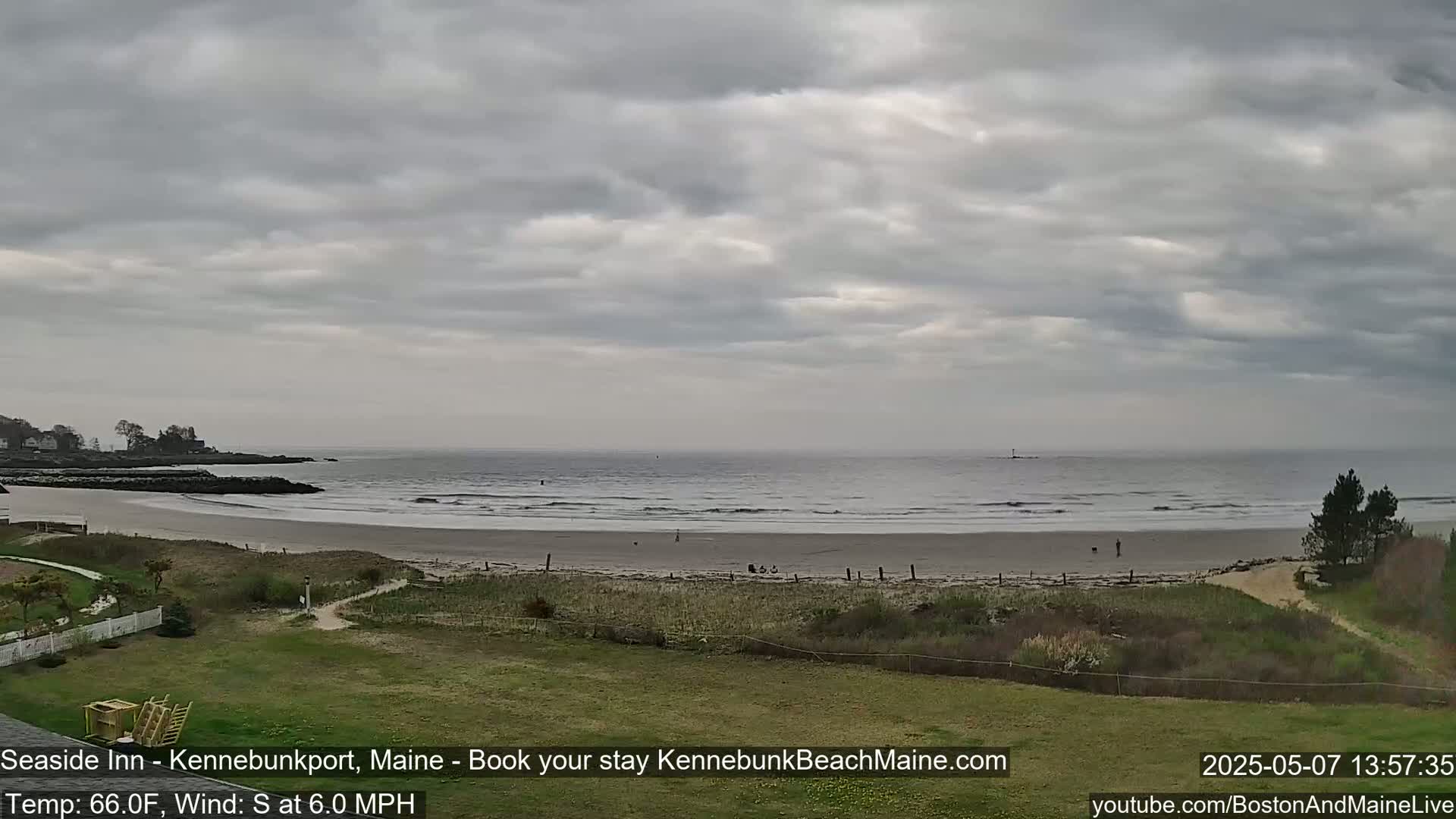 A mostly cloudy day at a sandy beach with a calm ocean, showing a few people walking along the shore.
