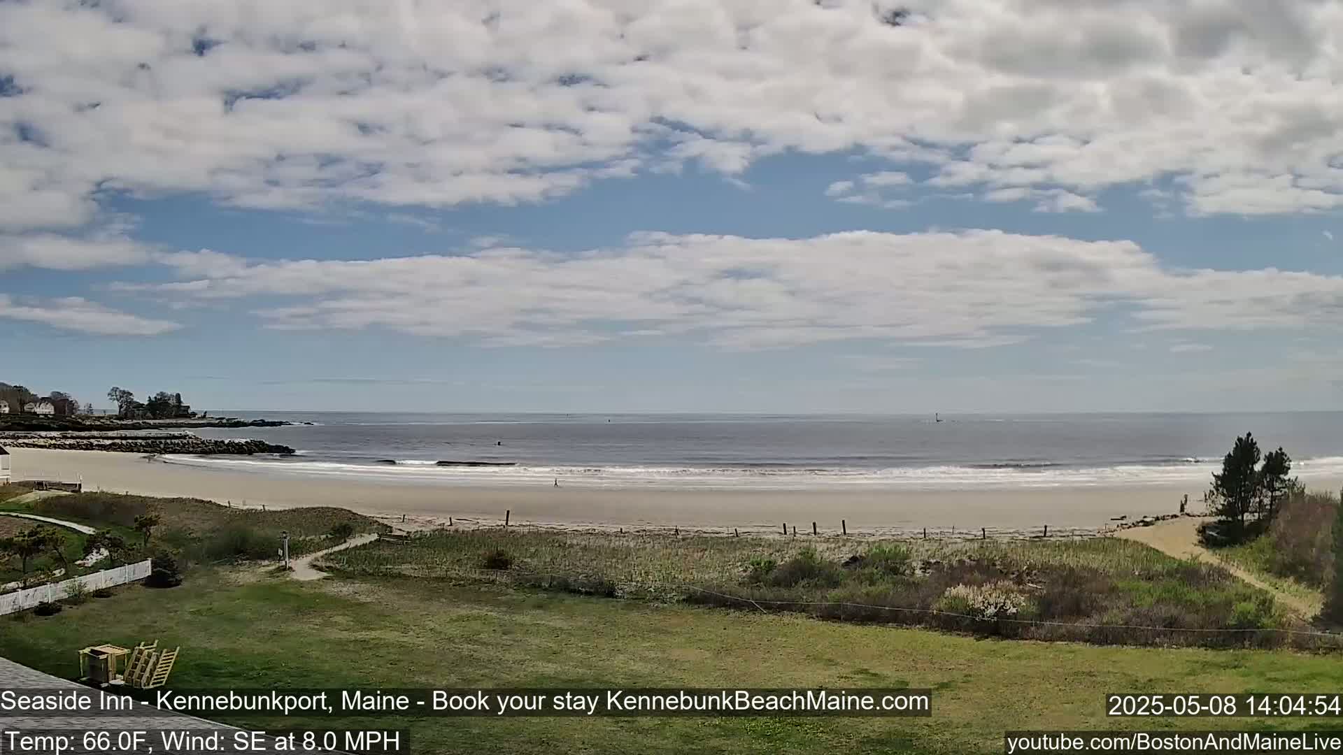 A sandy beach with gentle waves stretches to a calm ocean under a partly cloudy sky.