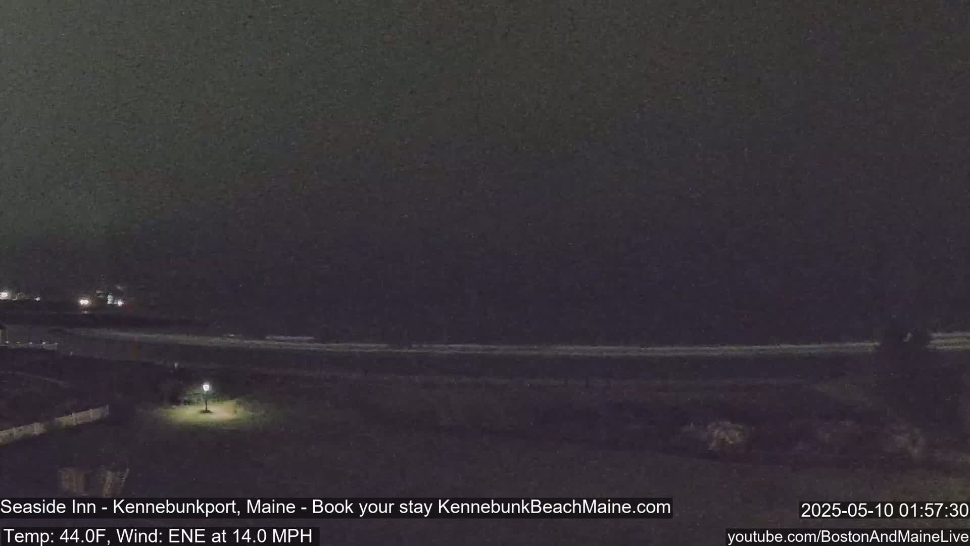 A nighttime view of a dark ocean shore with a single lamp illuminating a patch of grass.