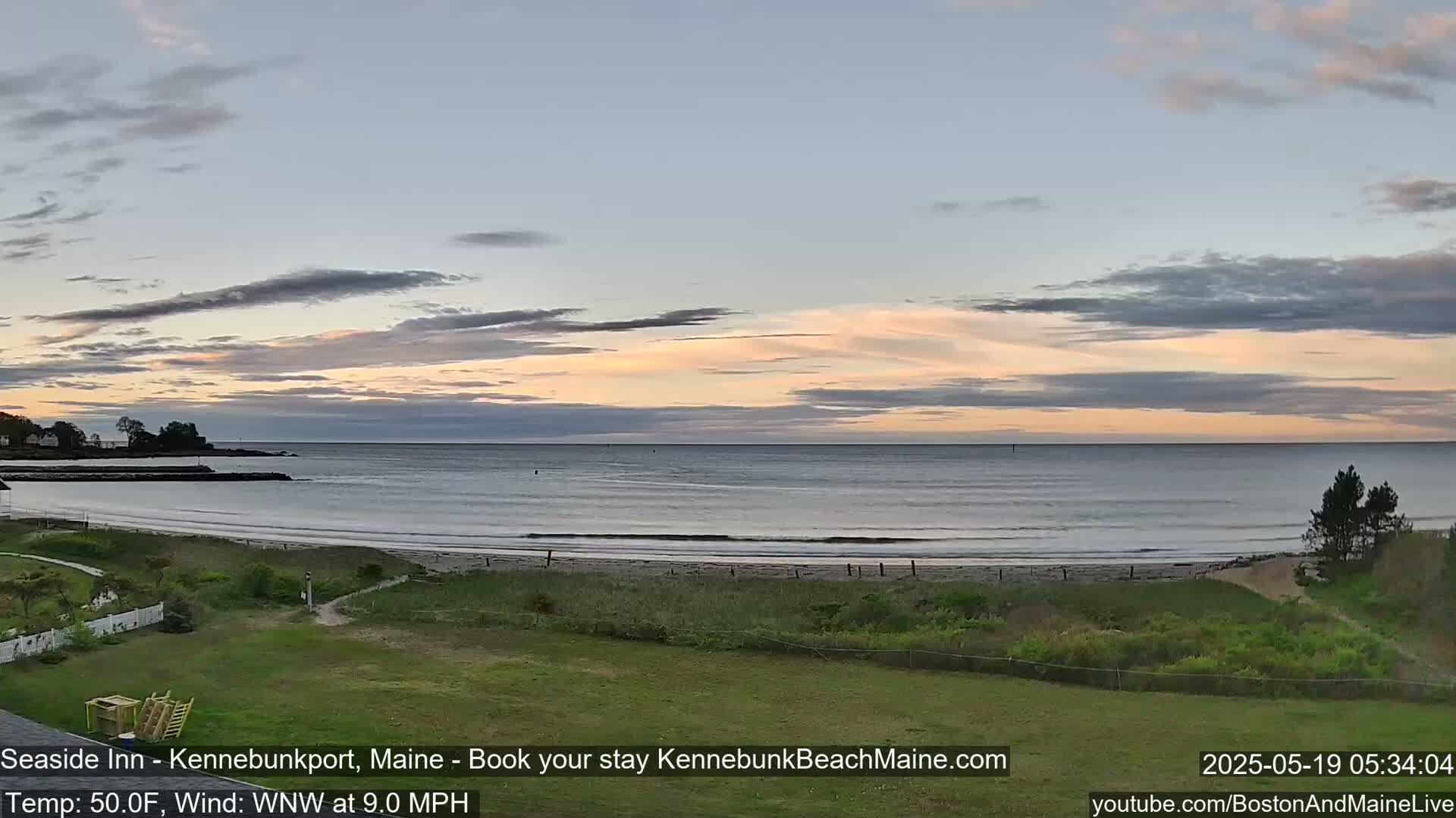 A calm ocean beach at dawn under a partly cloudy sky with a gentle wind.