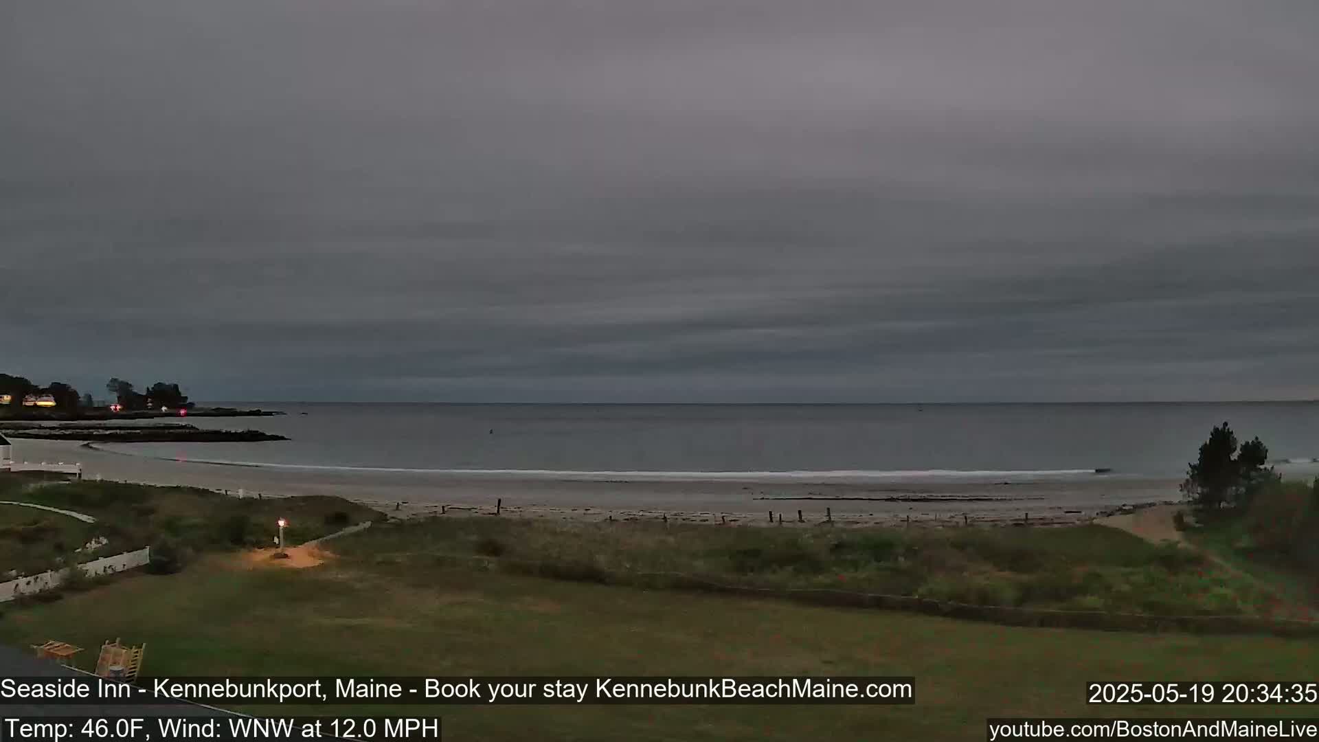A calm, overcast evening scene shows a sandy beach and ocean under a gray sky.