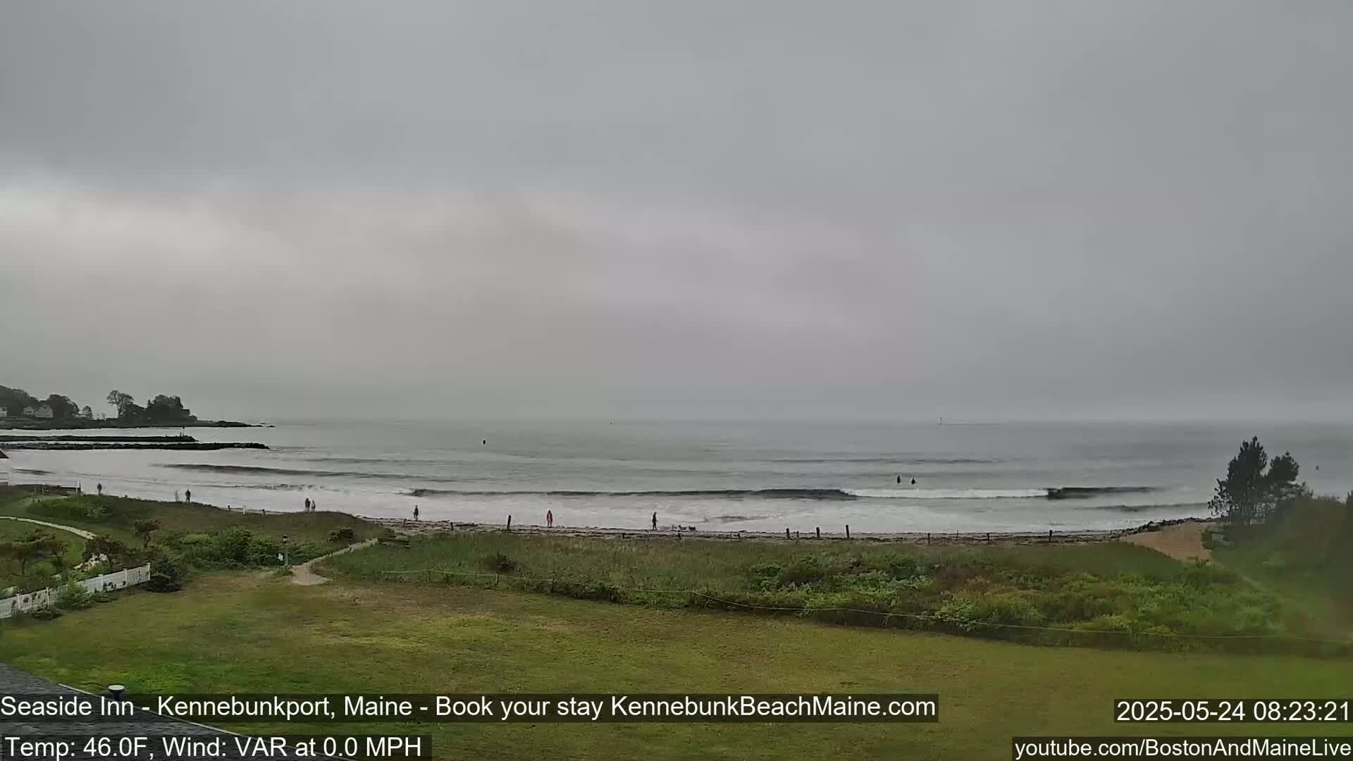A gray, overcast day at a beach shows a calm ocean with small waves and a few people on the shore.