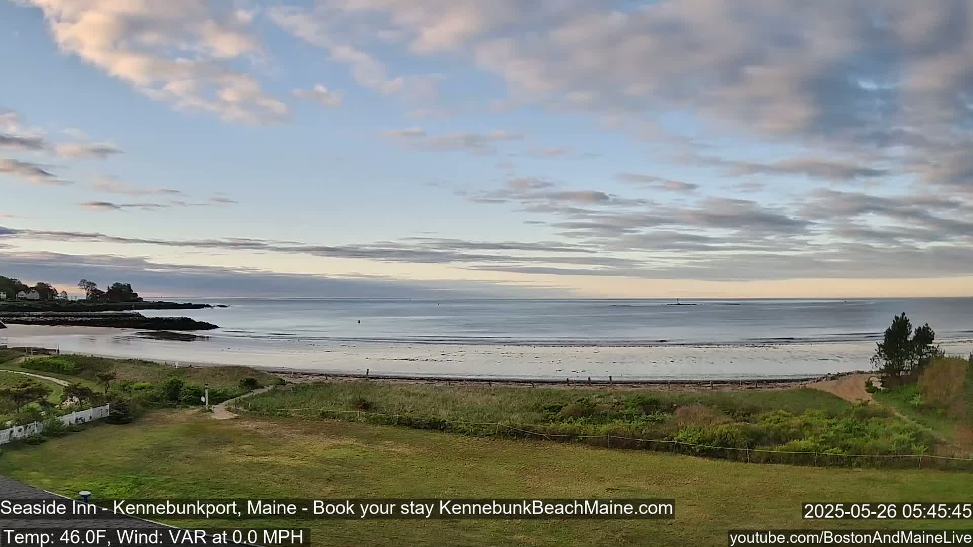 A calm ocean beach with a partly cloudy sky at dawn.