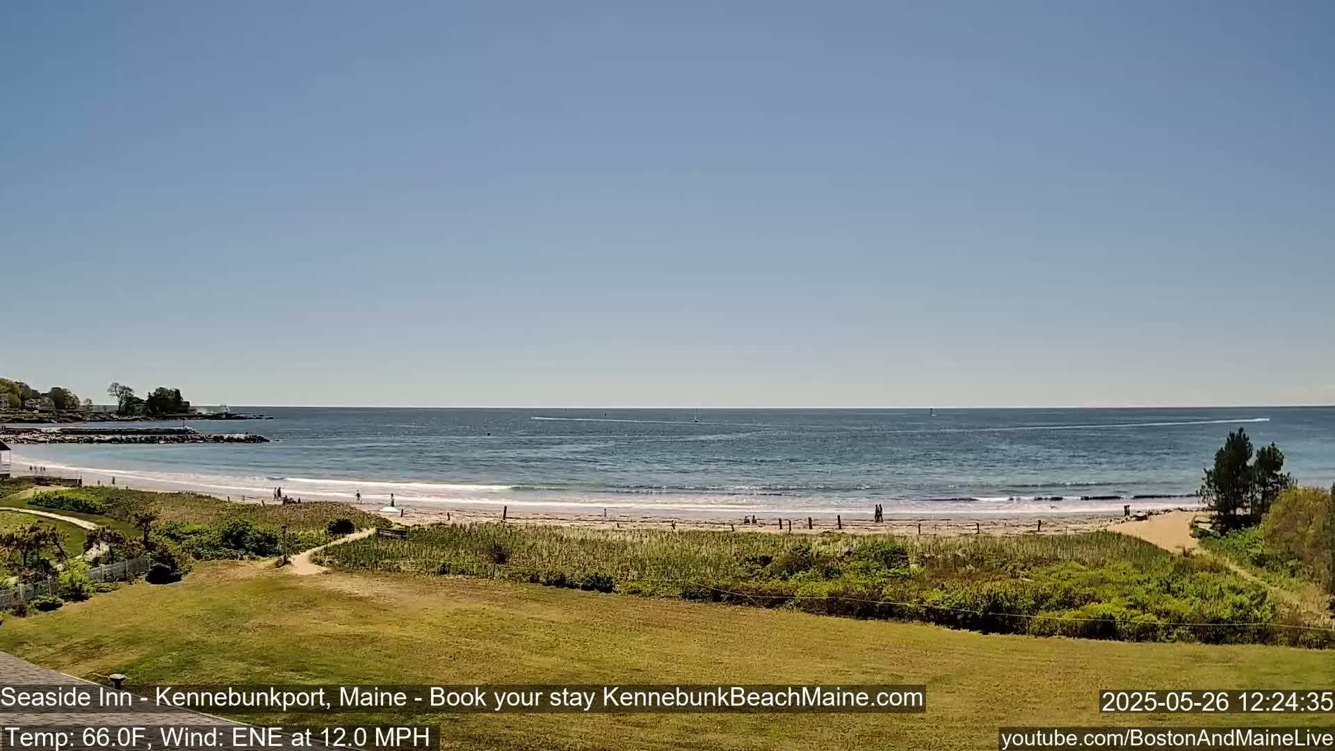 A sandy beach with a few people on it stretches along a calm ocean under a clear blue sky.
