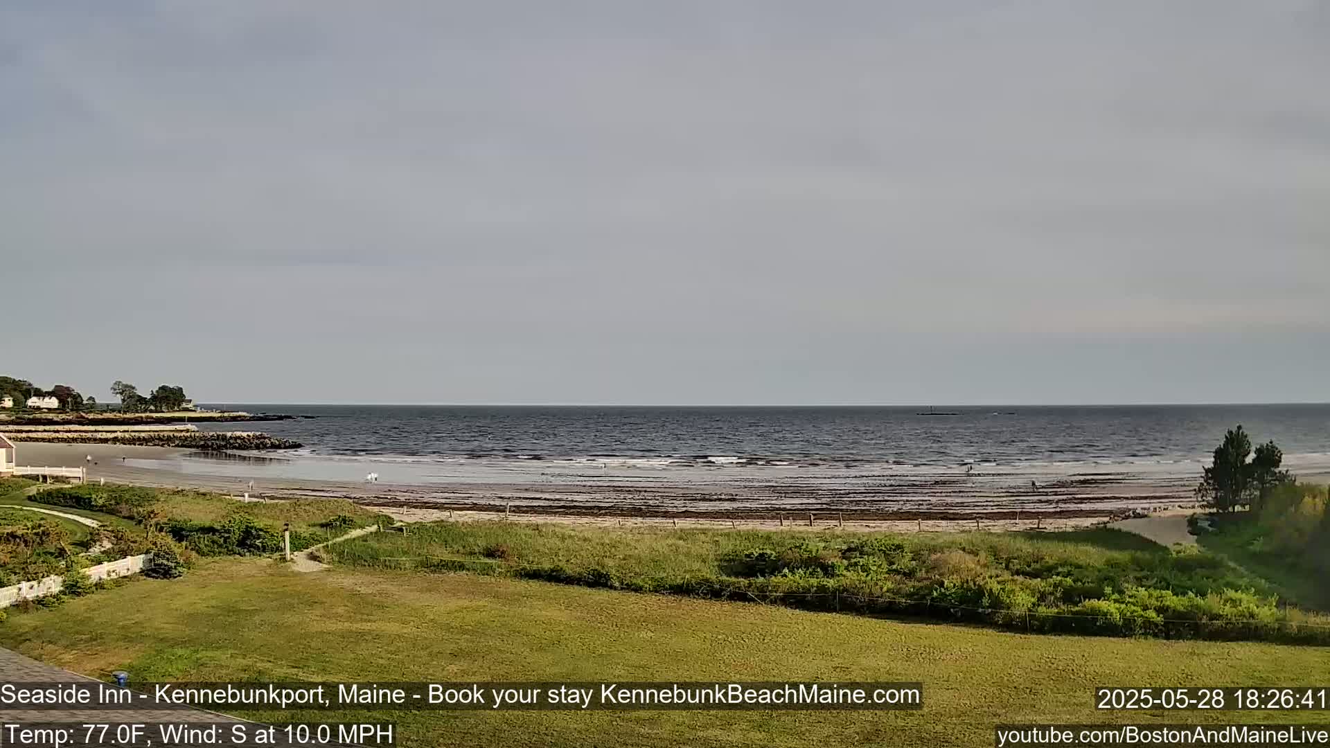 A sandy beach with calm ocean waves stretches out to a hazy horizon under a mostly cloudy sky.