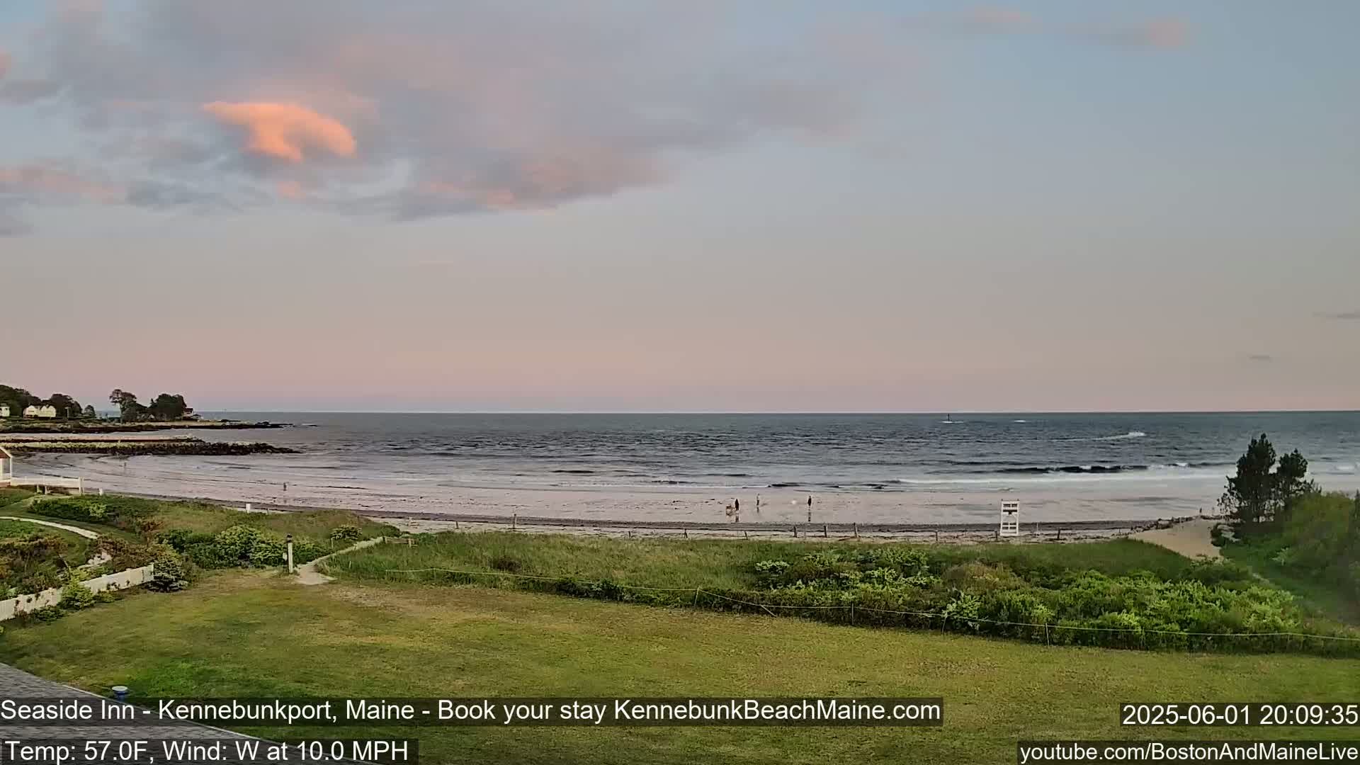 A calm ocean with small waves gently laps a sandy beach under a pastel sunset sky.
