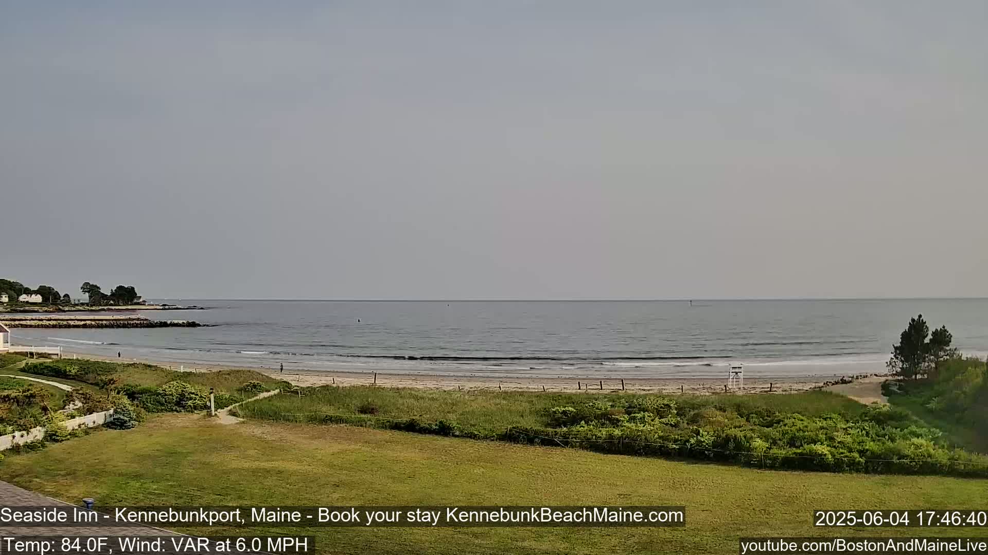 A sandy beach with calm ocean waves stretches along a coastline under a hazy sky.