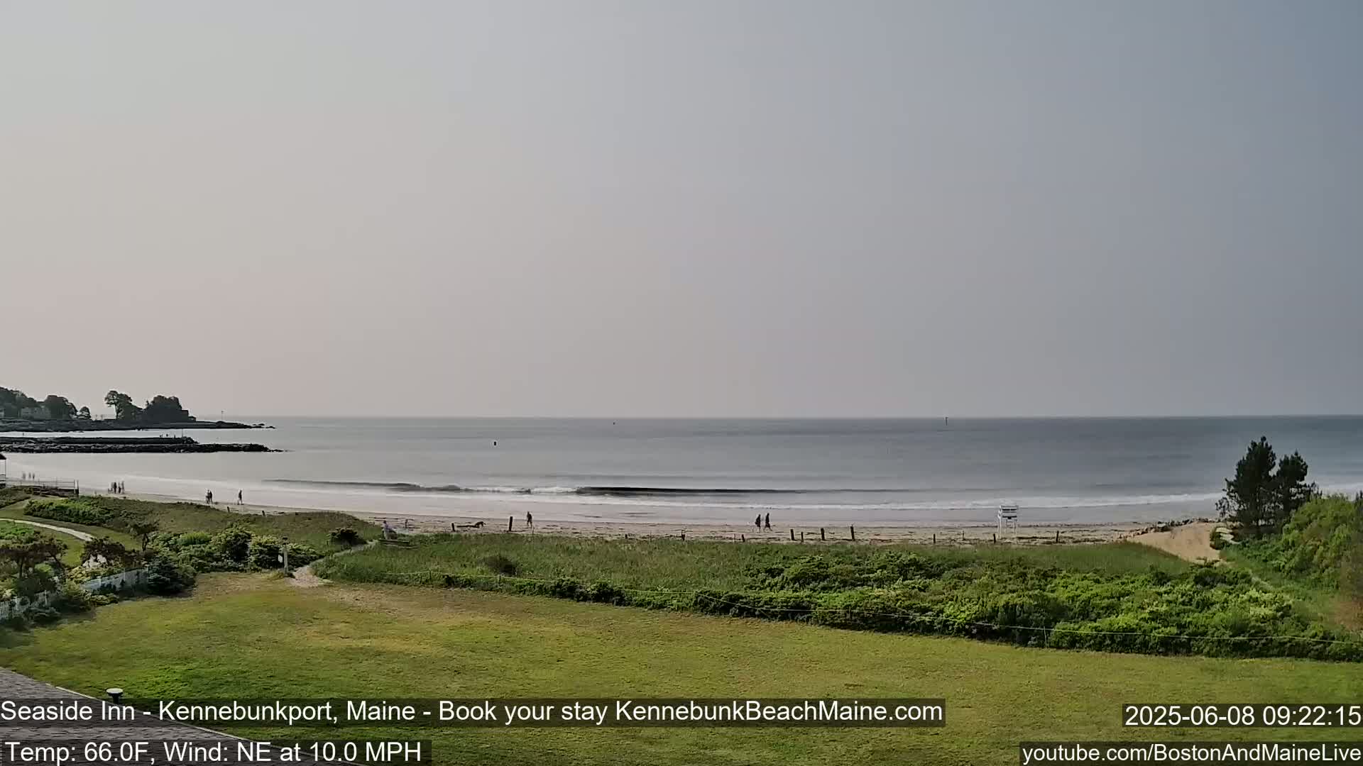 A calm ocean beach scene on a partly cloudy day with a gentle northeast wind shows a sandy beach with a few people, green vegetation, and a calm ocean.