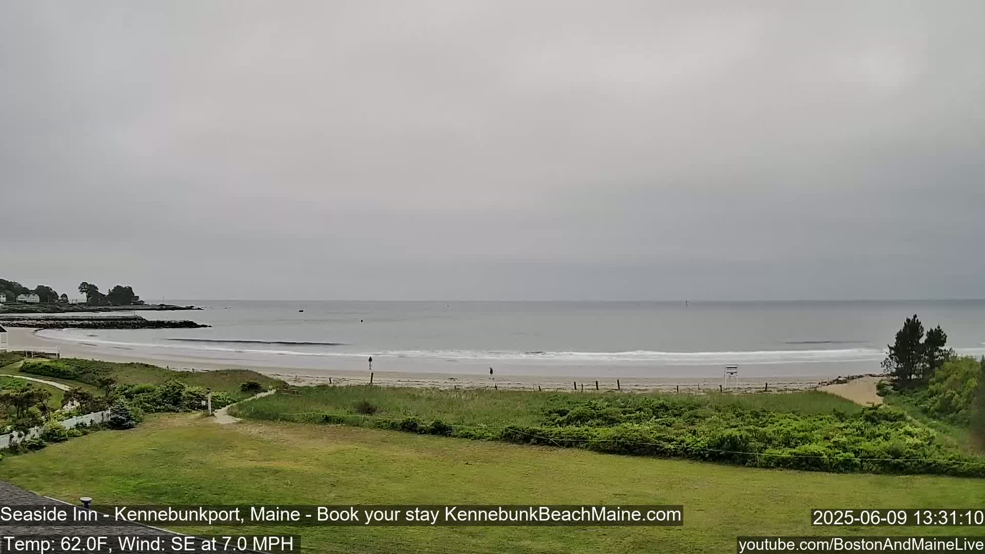 A sandy beach with gentle waves stretches along a calm, overcast ocean under a gray sky.