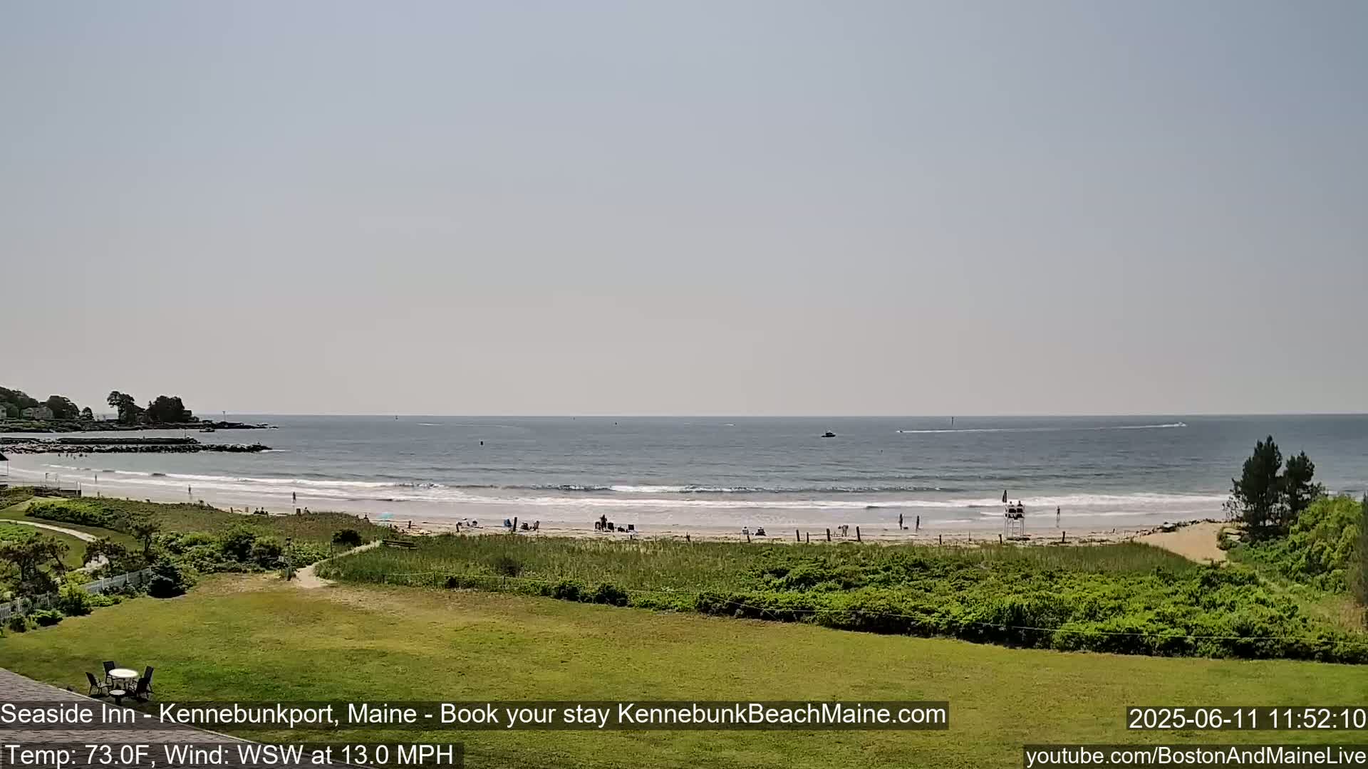A sandy beach with a few people on it is visible from an elevated vantage point, with calm ocean waves rolling in under a clear sky.