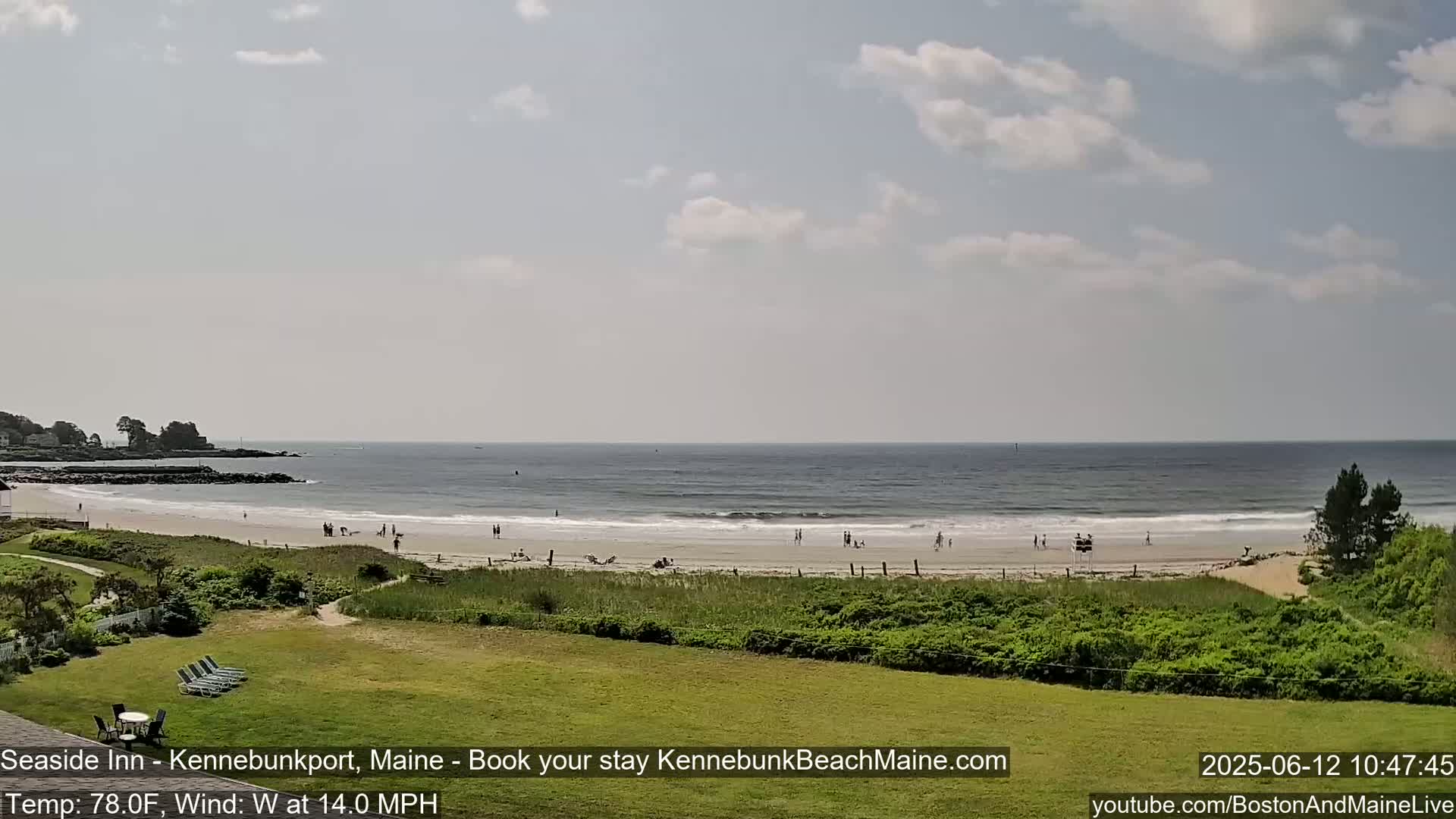 A sandy beach with a few people on it stretches along a calm ocean under a partly cloudy sky.