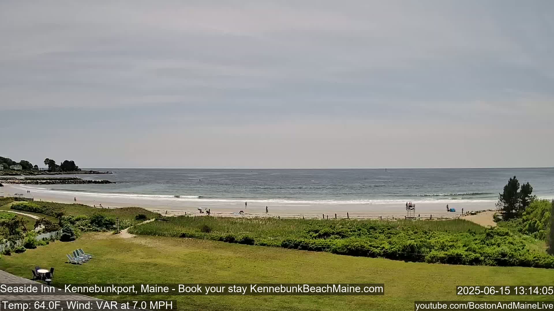 A sandy beach with a few people on it stretches along a calm ocean under a mostly cloudy sky.