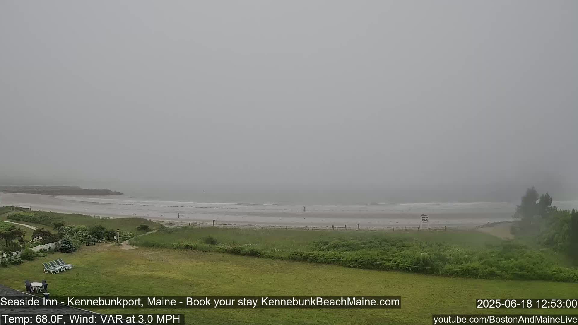 A foggy beach scene is visible from a grassy area, showing a calm ocean and a few people on the sand.
