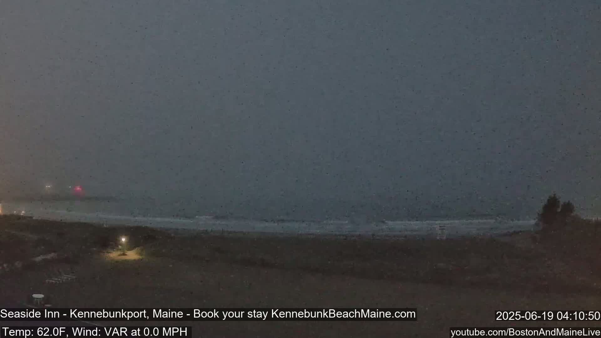 A dark, overcast beach scene shows a calm ocean under a heavy, gray sky.