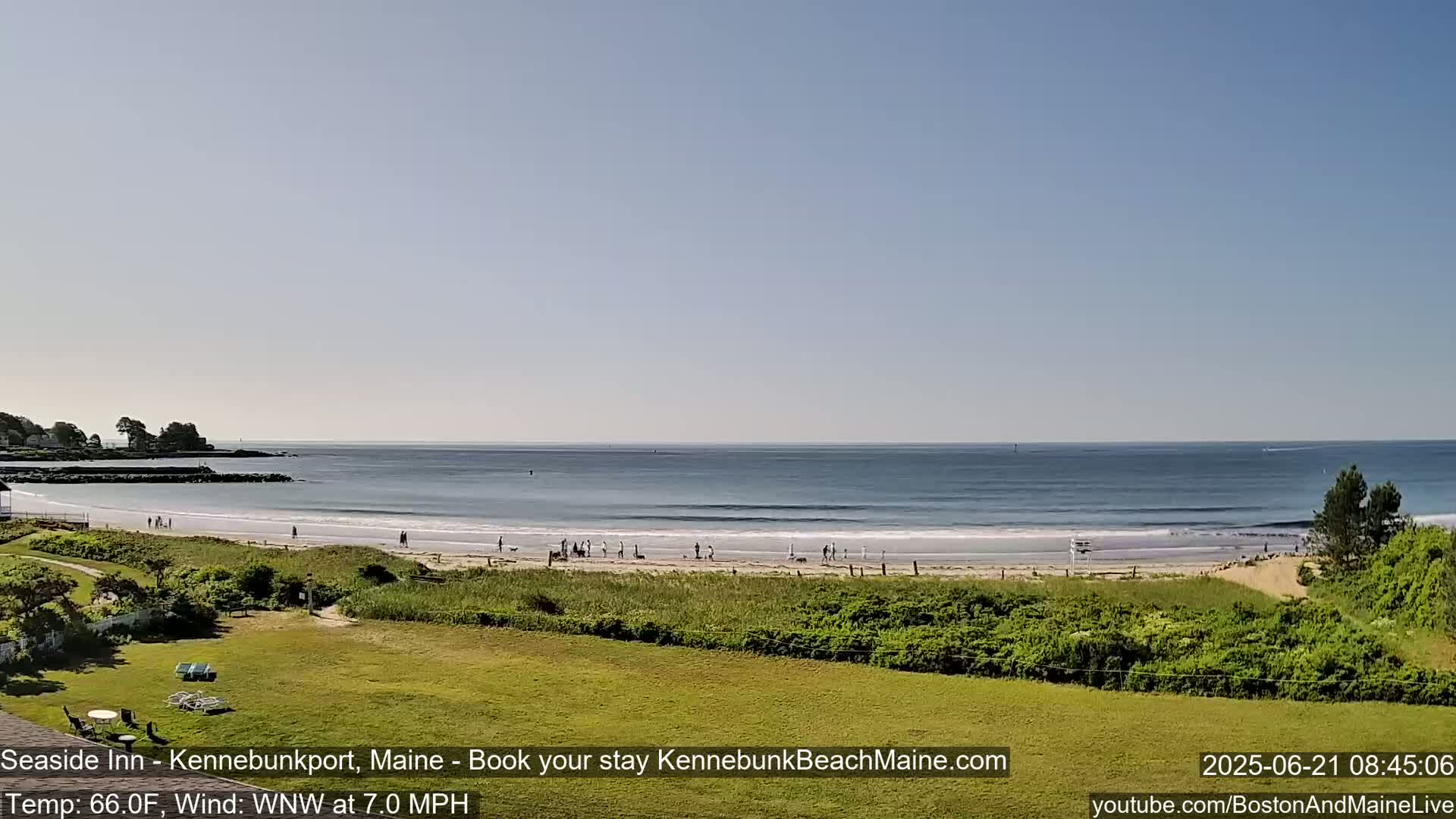 A sandy beach with a few people on it stretches along a calm ocean under a clear sky.