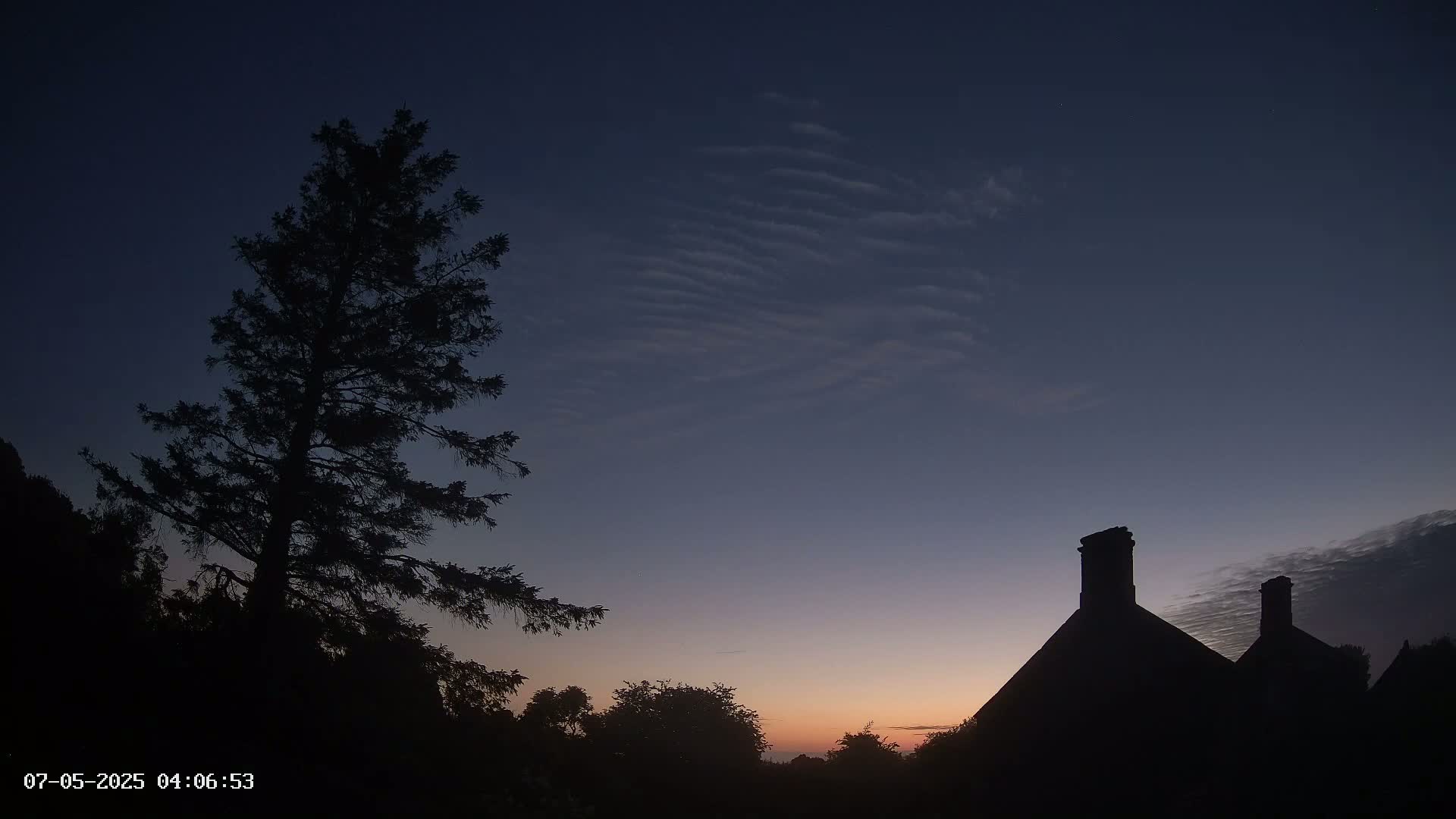 Silhouetted trees and a building with chimneys are visible against a twilight sky with thin clouds.