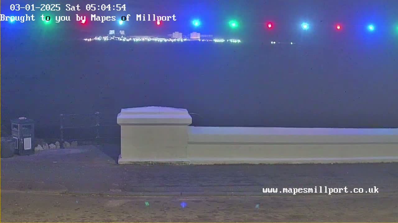 A hazy, nighttime view of a town's lights across a body of water, seen from behind a low white wall.