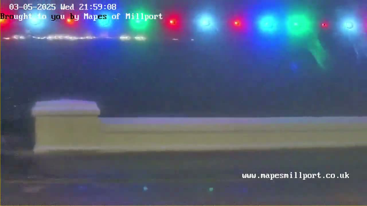 A low-lying, light-colored wall or barrier is visible in the foreground under a hazy, dark sky illuminated by a row of multicolored lights.
