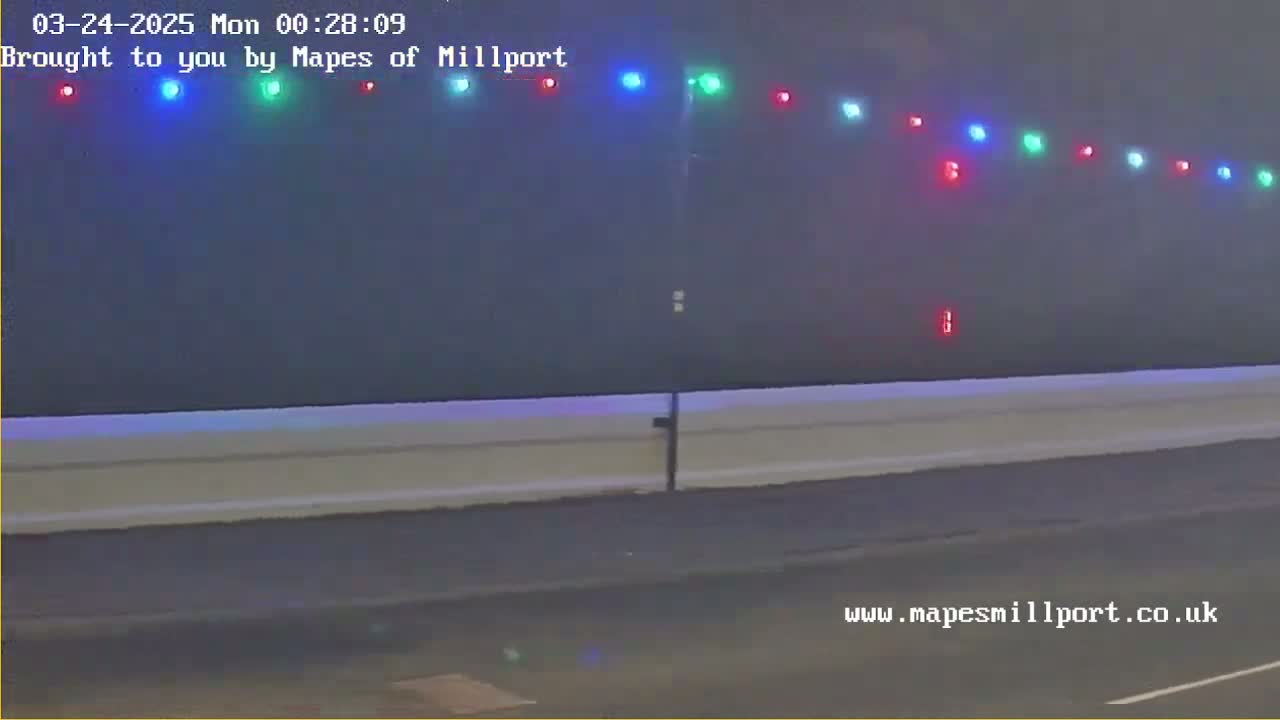 A nighttime outdoor scene shows a low wall with multicolored lights strung along the top, under hazy or foggy conditions.