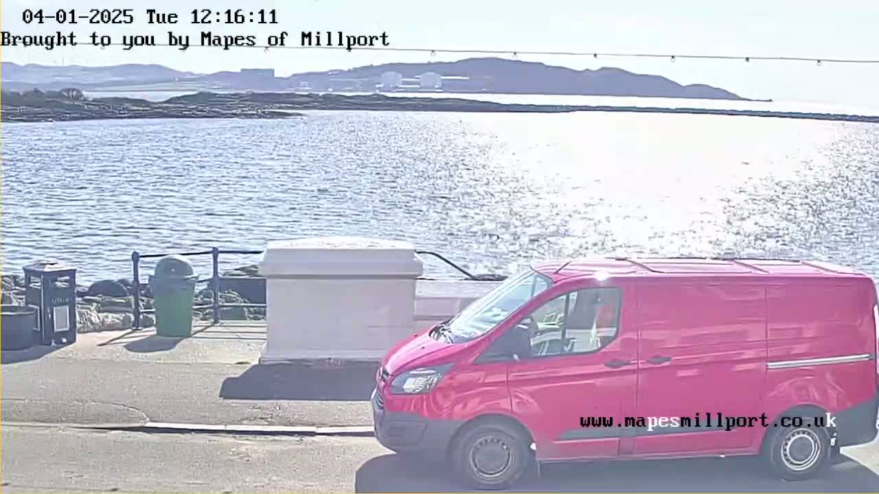 A red van is parked near a waterfront on a sunny day, with calm water and distant hills visible.
