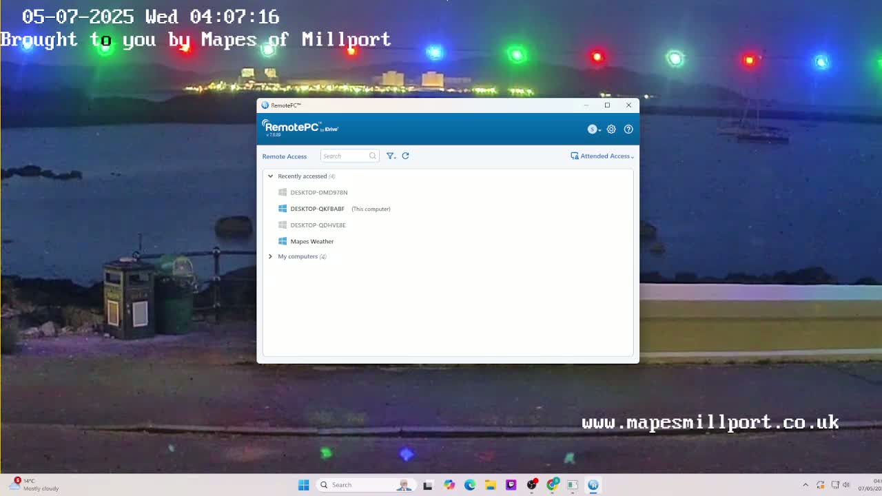A mostly cloudy night scene shows a waterfront with a low wall, a couple of trash receptacles, and colorful lights strung overhead; a computer screen displays a remote access program.