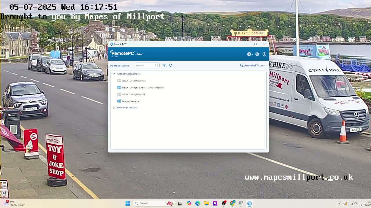 A mostly cloudy day shows a street scene with parked cars, a white van, and a toy and joke shop, viewed through a computer screen displaying a remote access program.