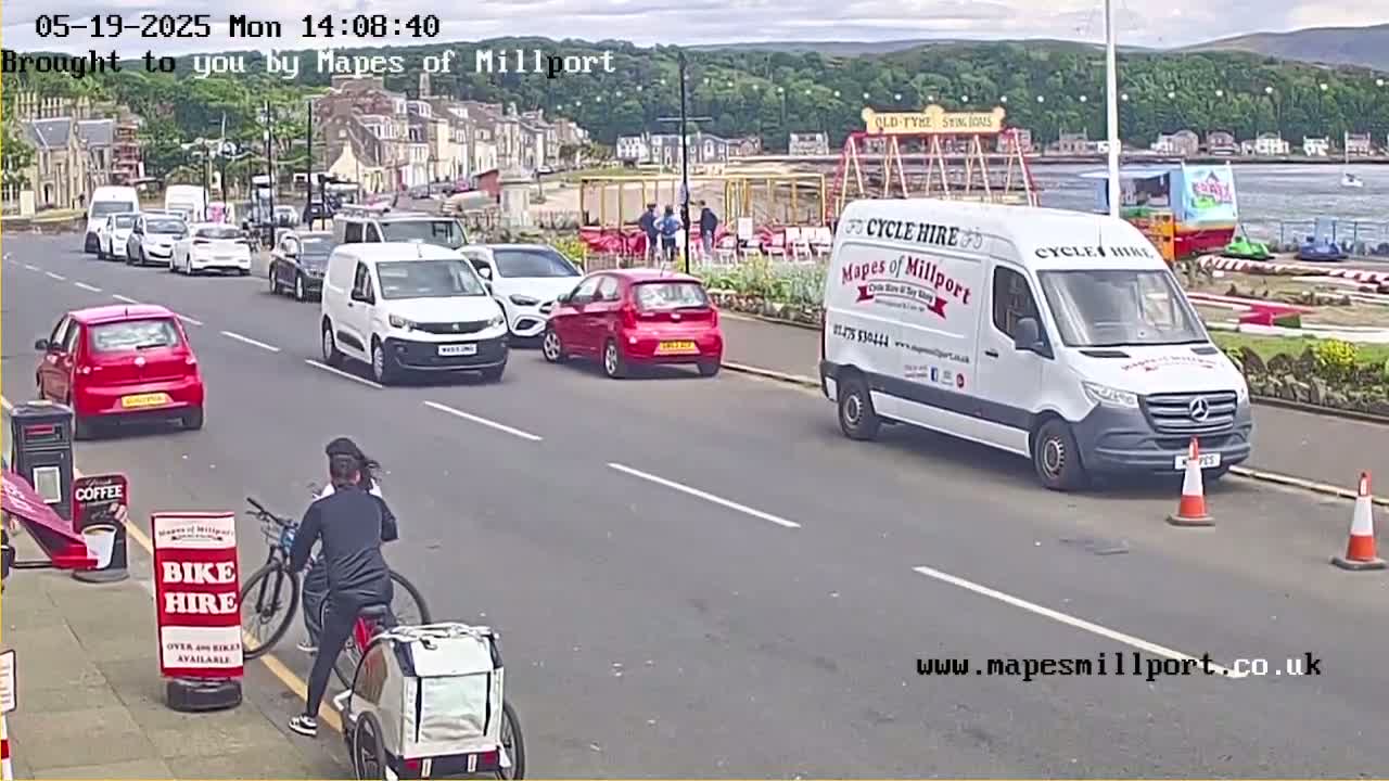 A person on a bicycle with a cargo trailer is near a street with parked cars and a white van, all under partly cloudy skies.