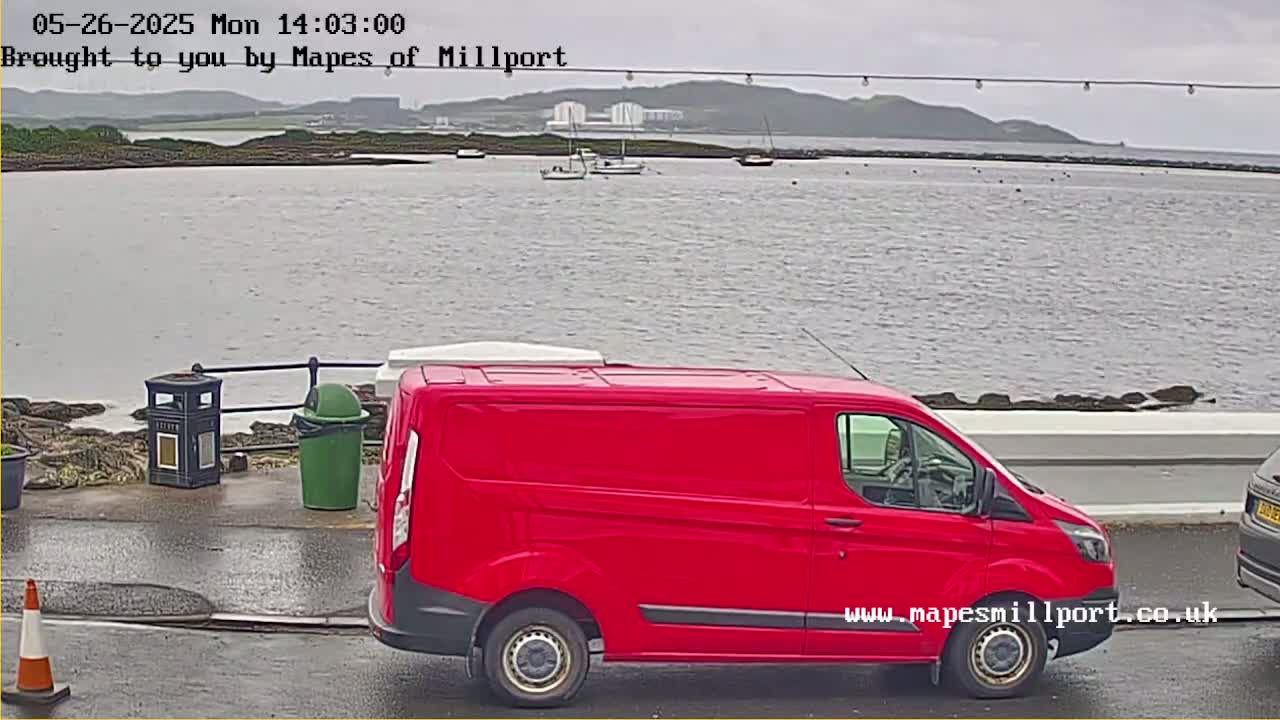 A red van is parked near a waterfront on an overcast day with several boats visible in the distance.