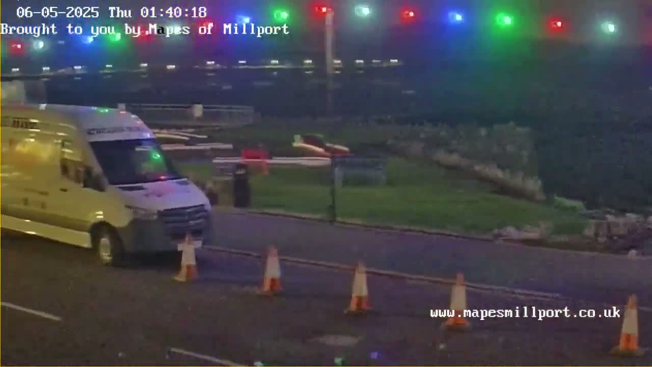 A white van is parked on a road at night under hazy conditions, with several orange traffic cones nearby.