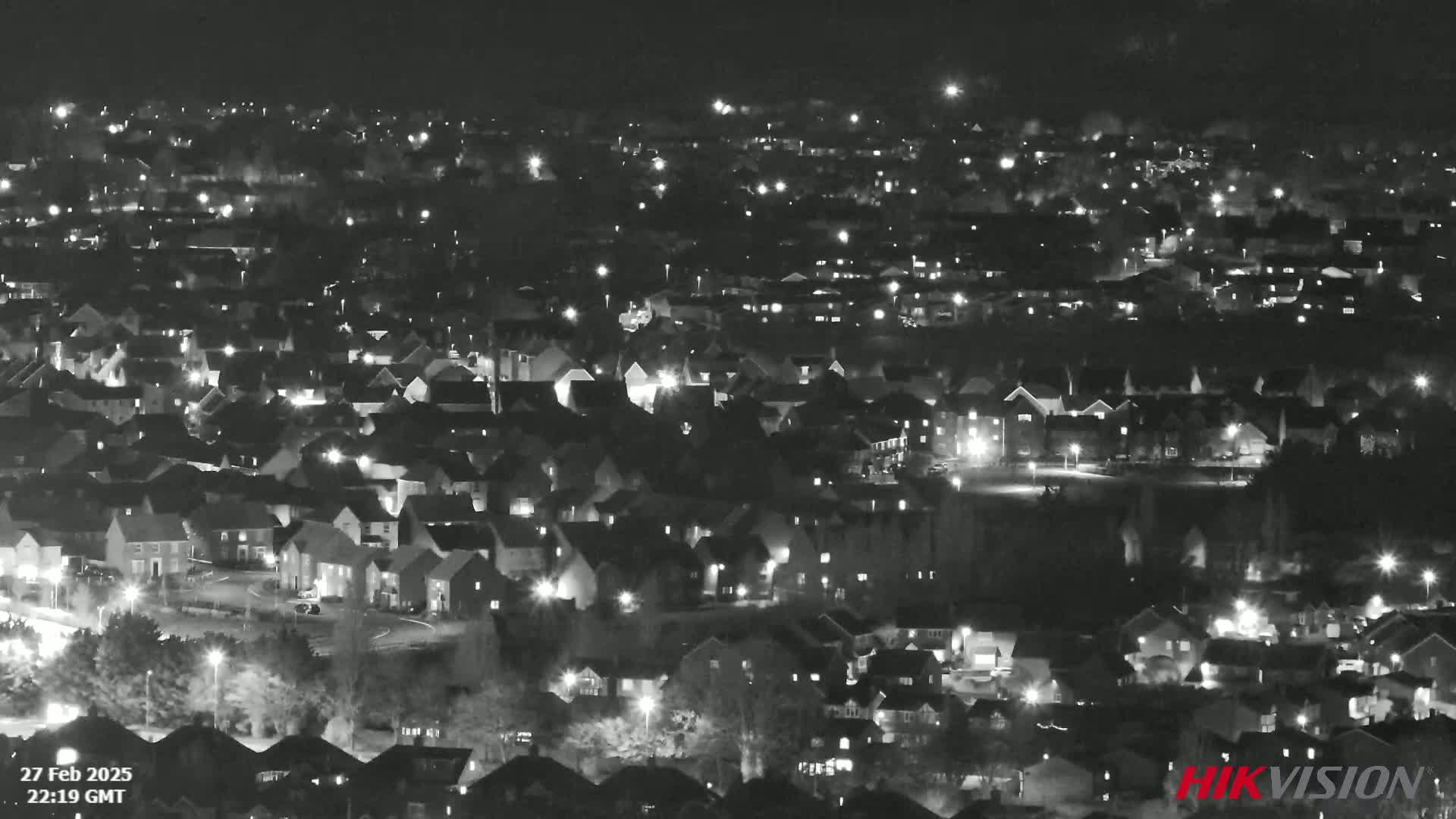 A nighttime, high-angle view of a sprawling residential area with numerous houses illuminated by streetlights and individual home lights.