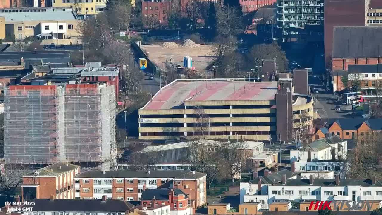 A high-angle, sunny-day view of a city, showing a multi-story parking garage, buildings under construction, and surrounding residential areas.