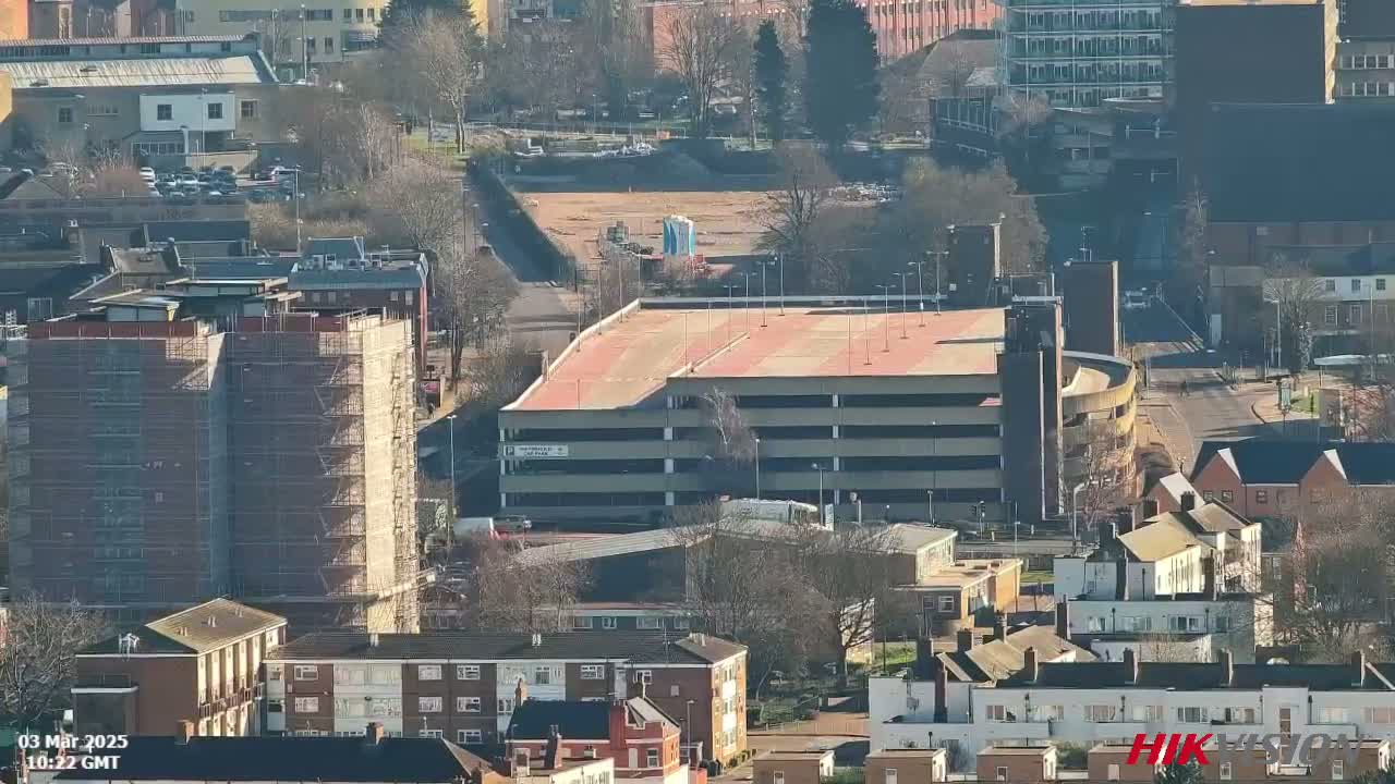A multi-story parking garage and surrounding buildings are visible on a sunny day, with one building under construction surrounded by scaffolding.