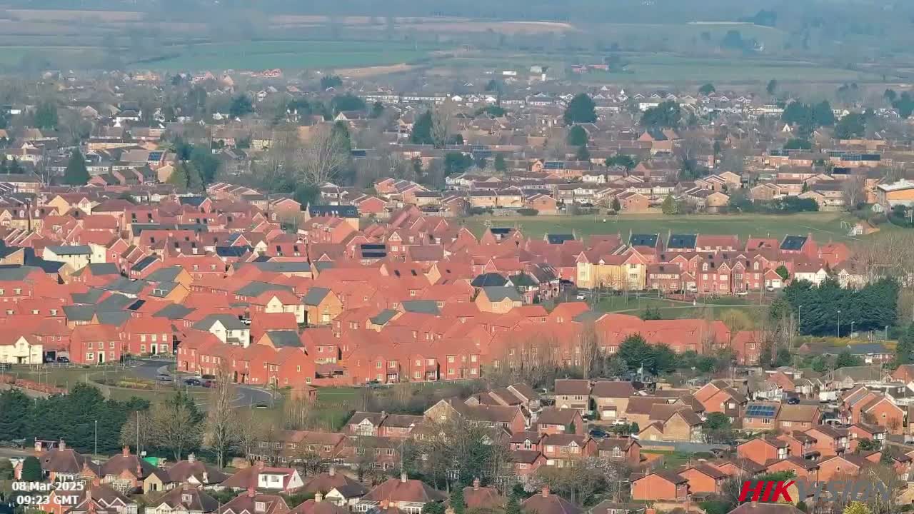 An expansive view of a residential area with many houses, predominantly featuring red-tiled roofs, under a clear, sunny sky.