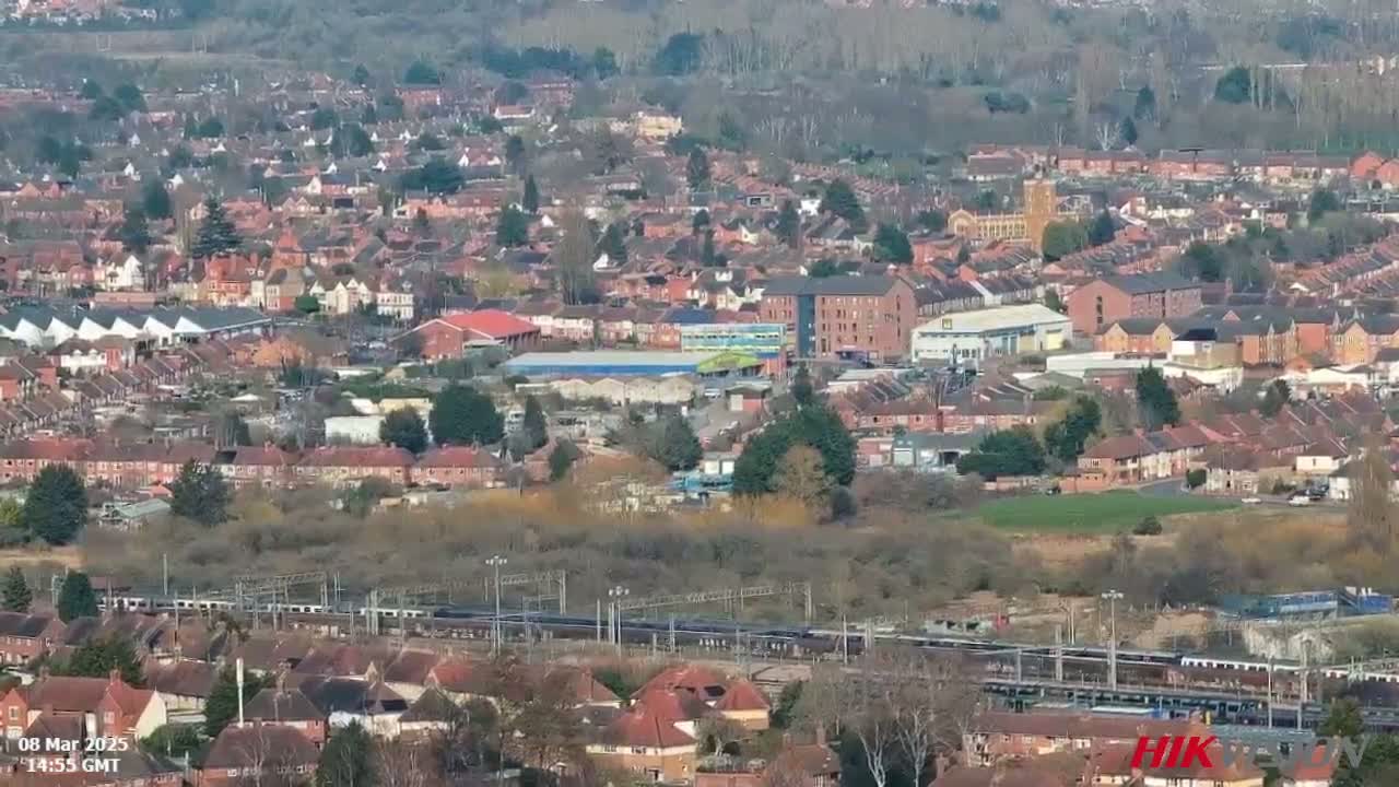 A sprawling residential area with a mix of houses and industrial buildings, traversed by a long freight train under a sunny sky.
