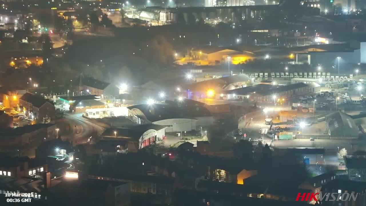 An aerial nighttime view of an industrial area with many buildings and vehicles, under hazy or foggy conditions.