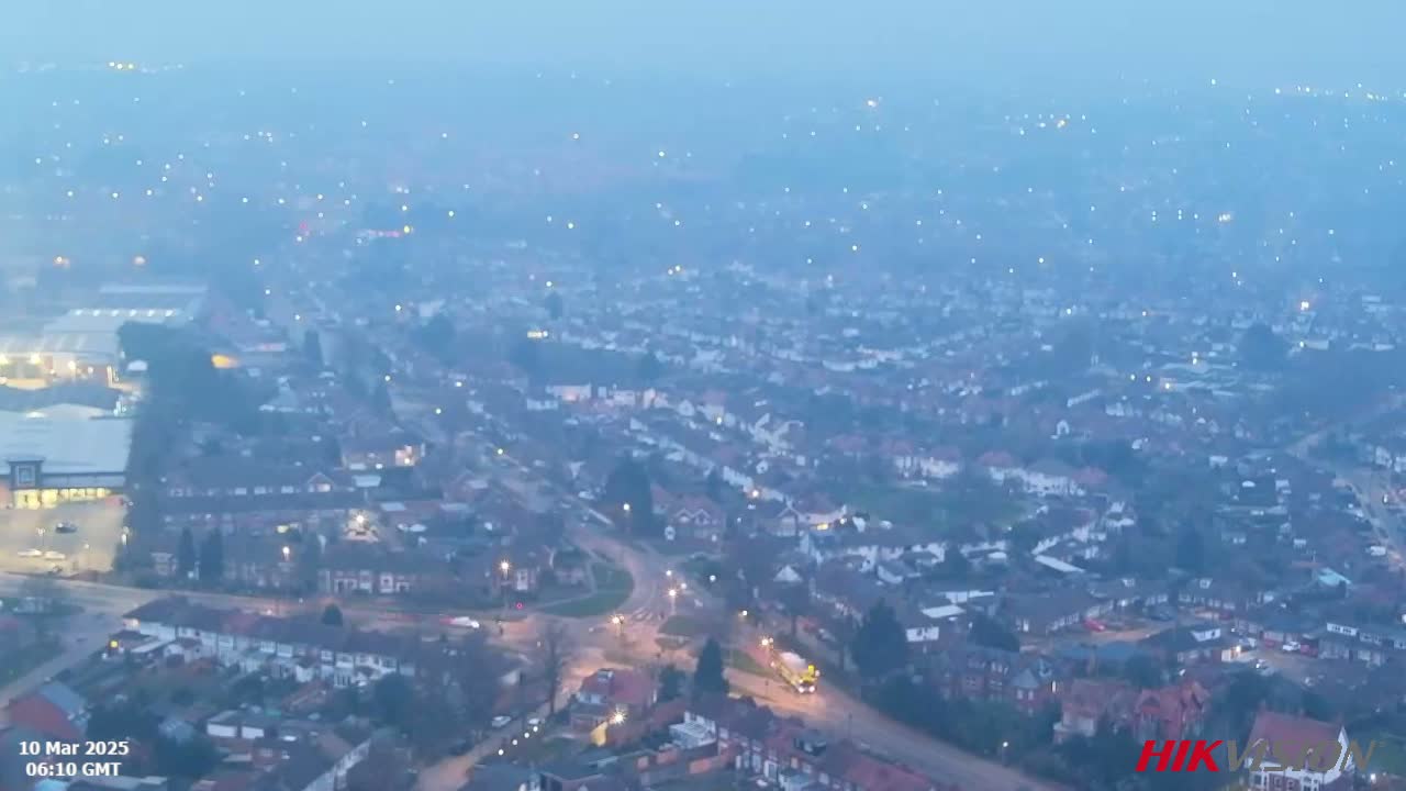 A hazy, dimly lit suburban area is viewed from above, showing many houses and roads at early morning.
