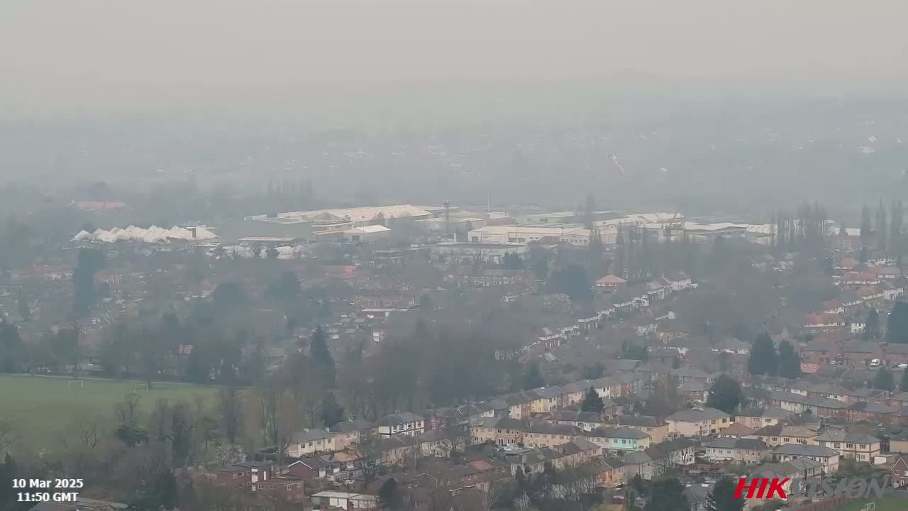 A hazy, overcast view shows a sprawling residential area with a large industrial complex in the background.