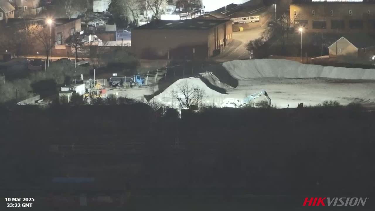 A nighttime view of an industrial area with construction equipment operating near piles of aggregate material under artificial light.